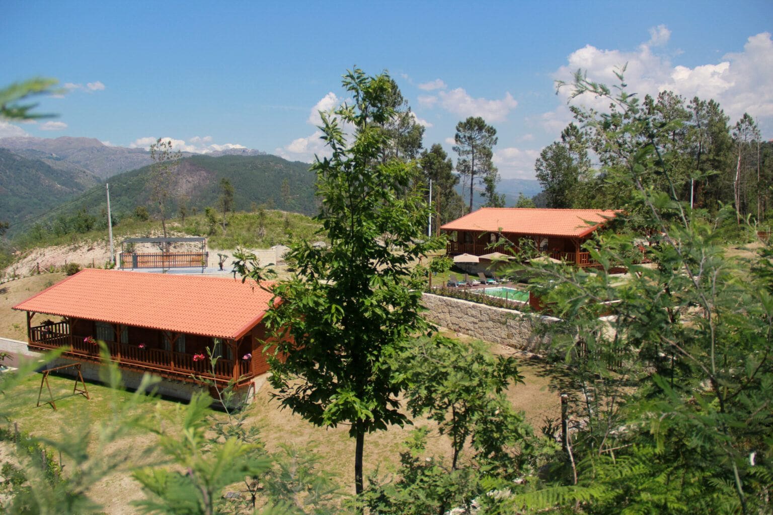 Os dois chalés de telhado vermelho entre árvores, com a serra ao fundo